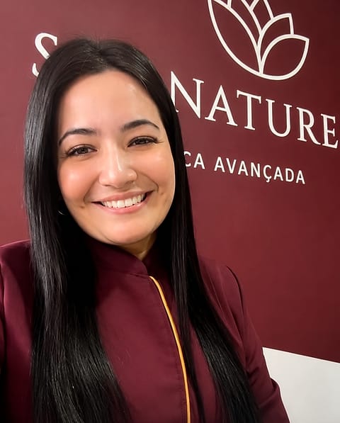 Talita Fernanda Soares, proprietária da SPA Nature Tijucas, sorrindo diante da parede com a marca da clínica